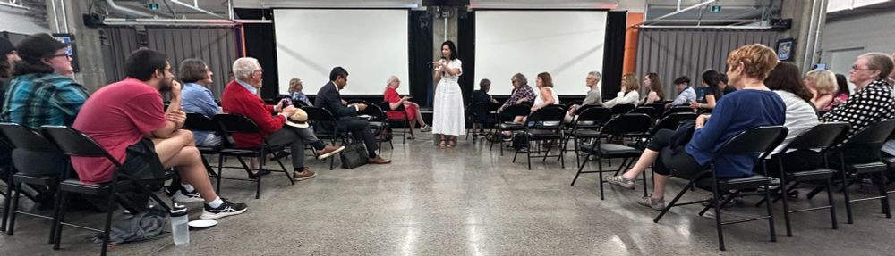 Joanne Chianello, standing, with the Champlain Park Community Association provides an update on community happenings to people seated in an large, open industrial space.