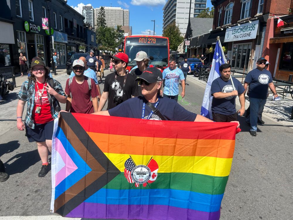 A member of ATU marches with a union flag in front of a bus displaying ATU 279 on its sign.
