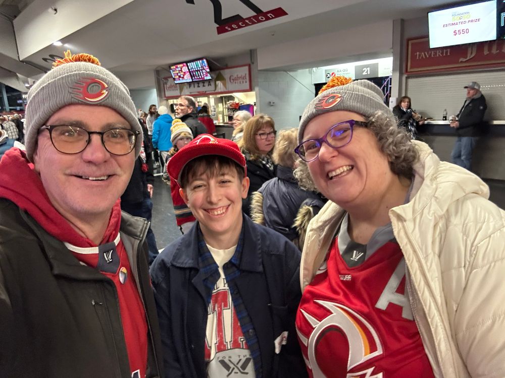 Nat and Jeff with Jeff’s assistant Steph pose for a selfie on the arena concourse / Nat et Jeff, accompagnés de Steph, l'assistante de Jeff, prennent un selfie dans le hall de l'arène.