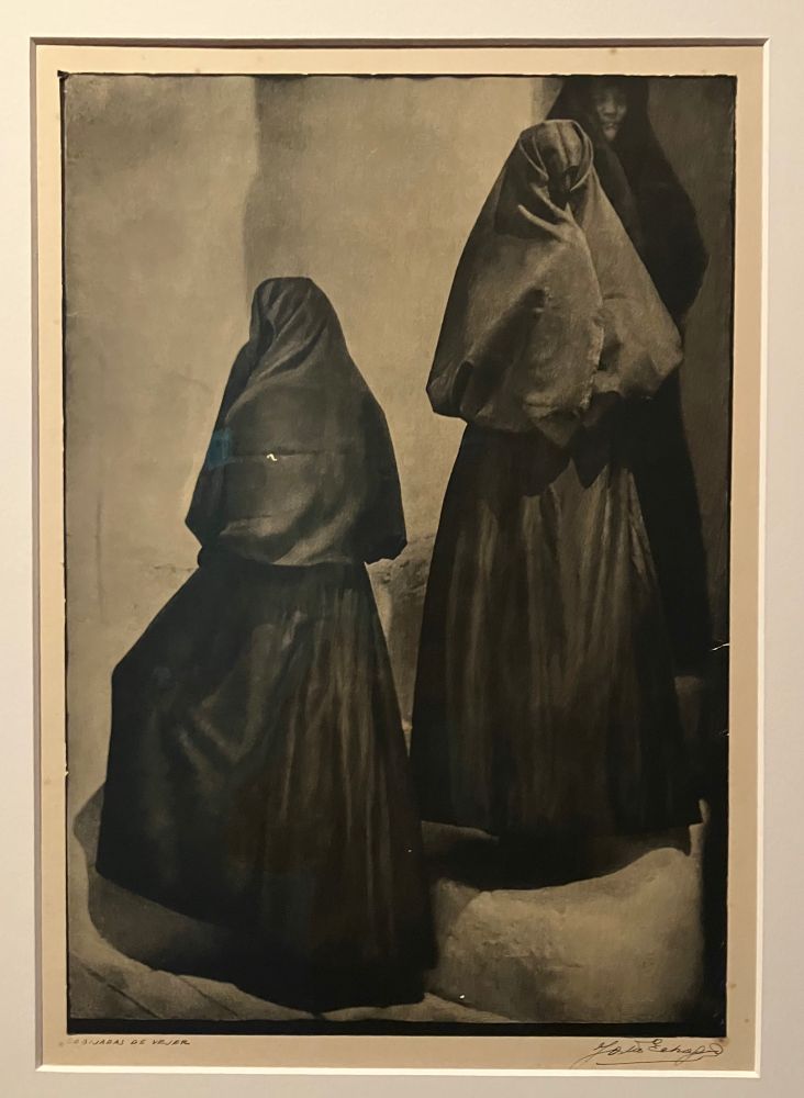 Fotografía en blanco y negro con dos mujeres, una de pie y otra sentadas, cubiertas de cabeza a los pies sí que se vislumbre un centímetro del cuerpo a la manera de un burka. 