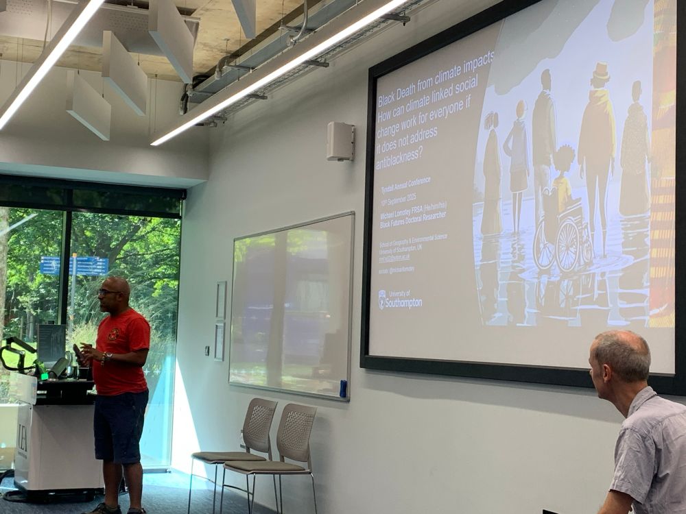Michael at the start of his provocation with a title slide pictured with art of a diverse group of black people including a person in a wheelchair. The title is “Black Death from climate impacts: How can climate linked social change work for everyone if it does not address antiblackness?”