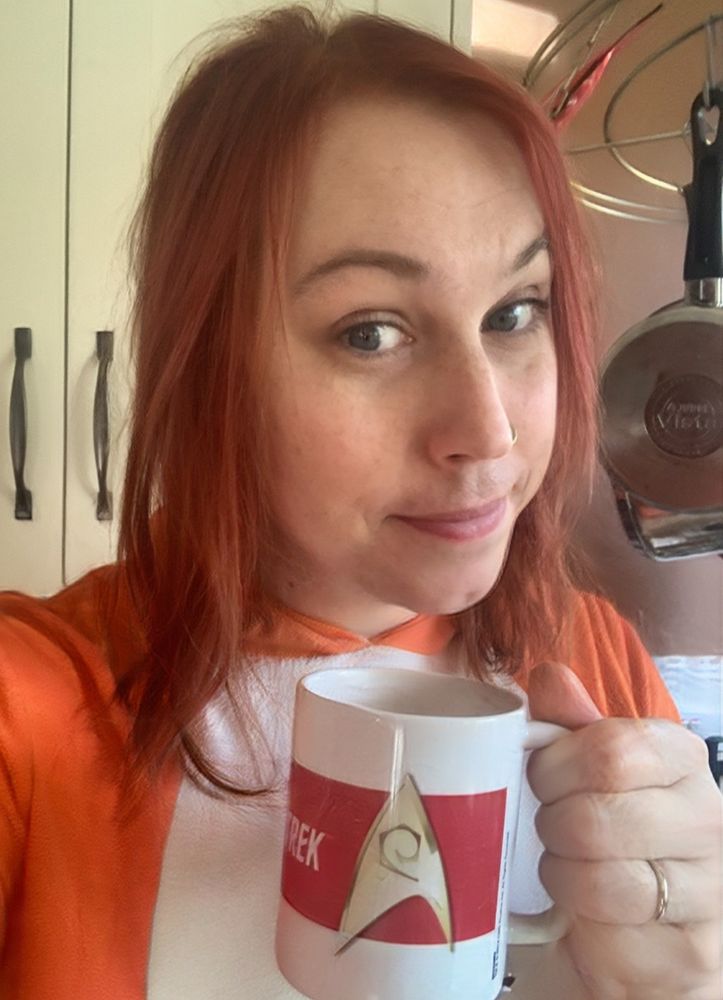Selfie drinking tea out of a white and reg mug with the Star Trek Starfleet delta on it