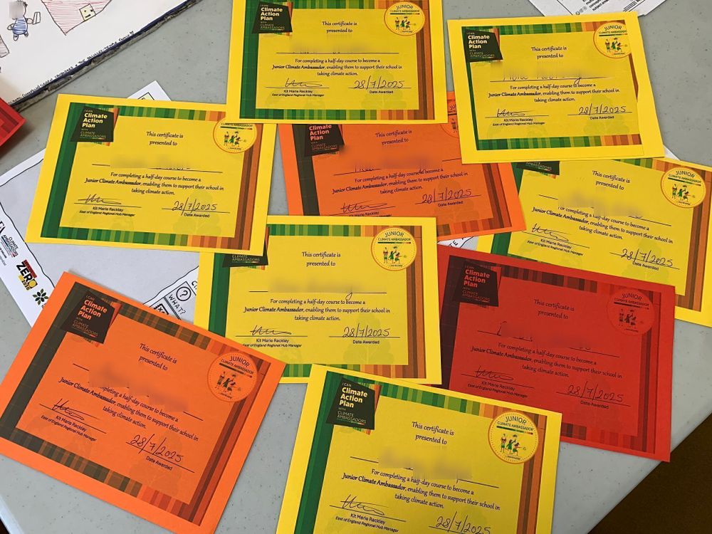 A collection of yellow and orange certificates laid out on a table, each awarded for completing a climate action ambassador training session.