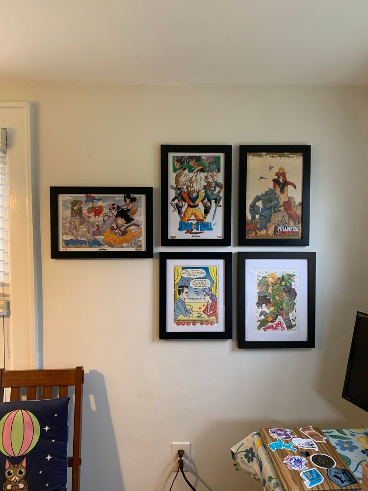In-progress gallery wall that includes (clockwise from left) a Dragon Ball poster, a Dragon Ball Z poster, a Fullmetal Alchemist poster, Dorohedoro art, and a Love Man print, all framed.