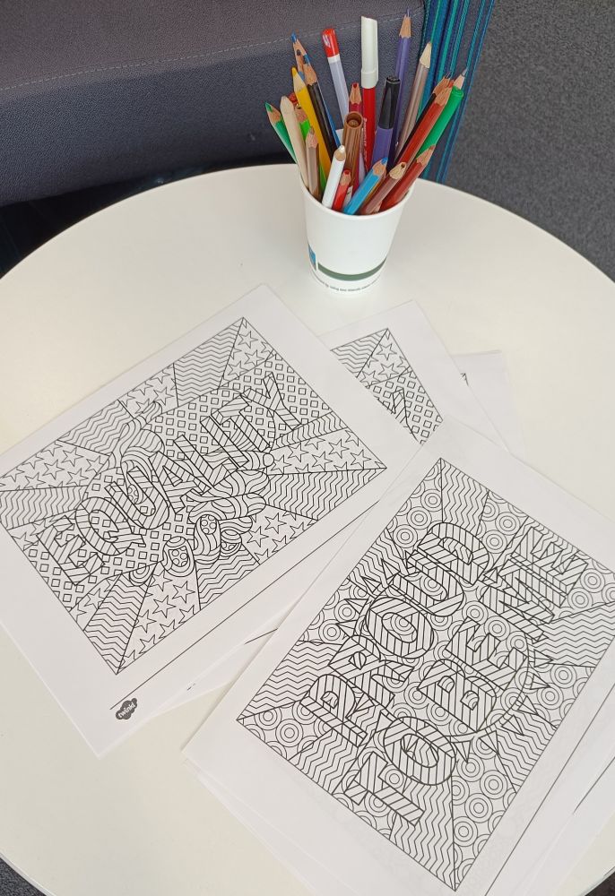 Colouring in sheets saying Proud To Be Me and Equality, with a pot of colouring in pens and pencils 