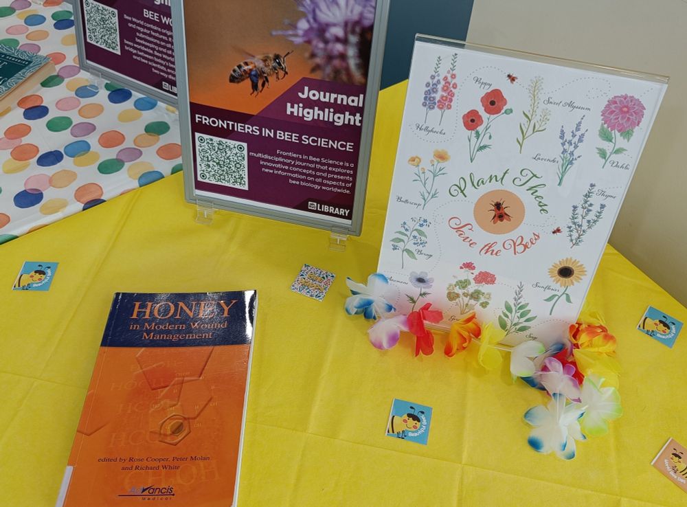 A poster encouraging planting flowers with a colourful garland round it's base, next to a book about honey