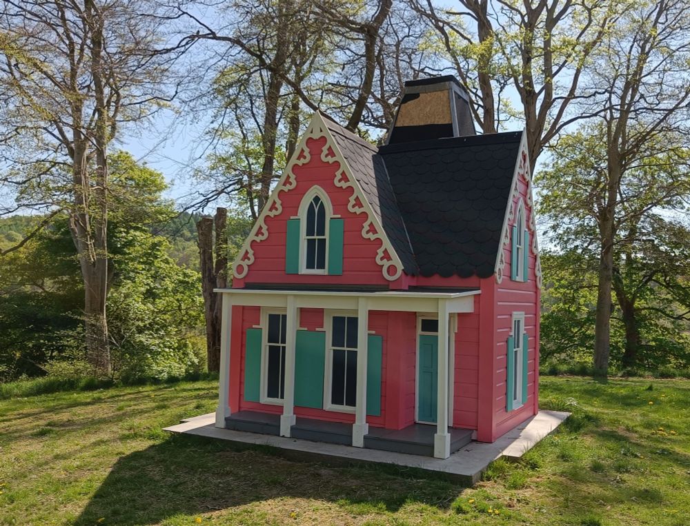 Front of the Little House in the Woods artwork which is a pink house with white features and green blinds outside each window