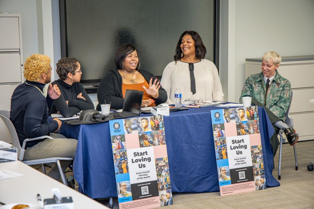 Five panelists laugh and listen, seated behind two "Start Loving Us" posters