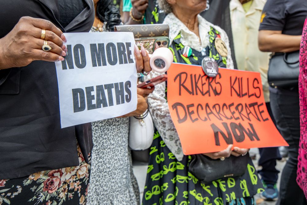 Advocates hold signs reading "No more deaths" and "Rikers kills, Decarcerate Now"