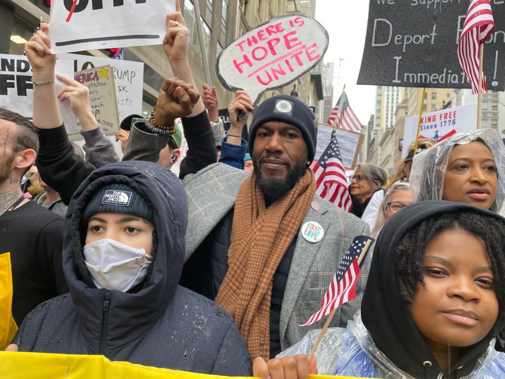 The Public Advocate smiles and raises a fist, under a sign reading, "There is Hope, Unite."
