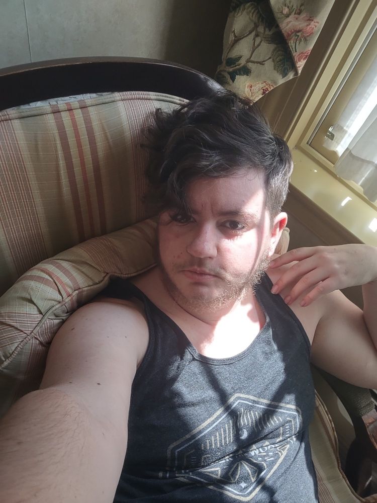 A beardy guy with eyeliner lounges in a chair