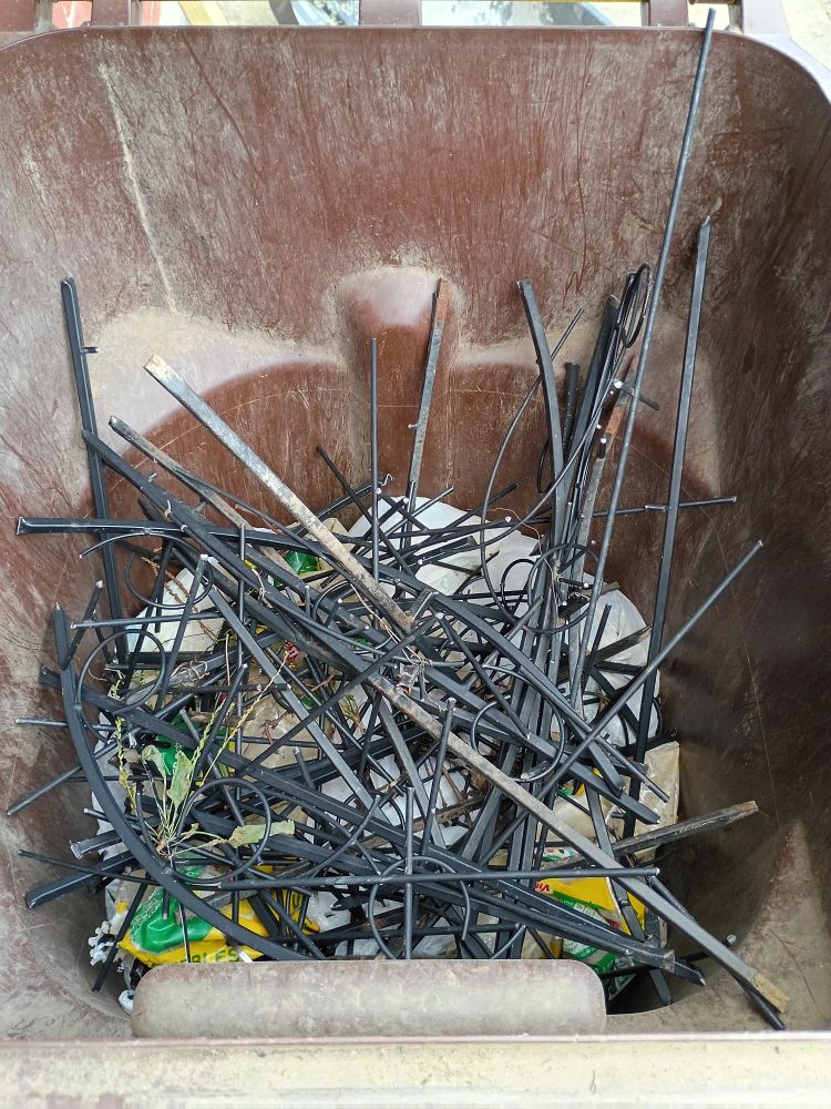 A trash can with several cut apart metal trellis pieces on top of trash bags.
