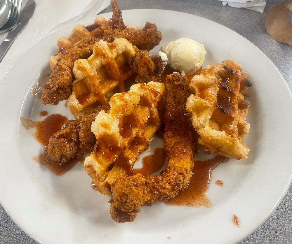 Plate of chicken tenders and a Belgian waffle covered in hot honey.  