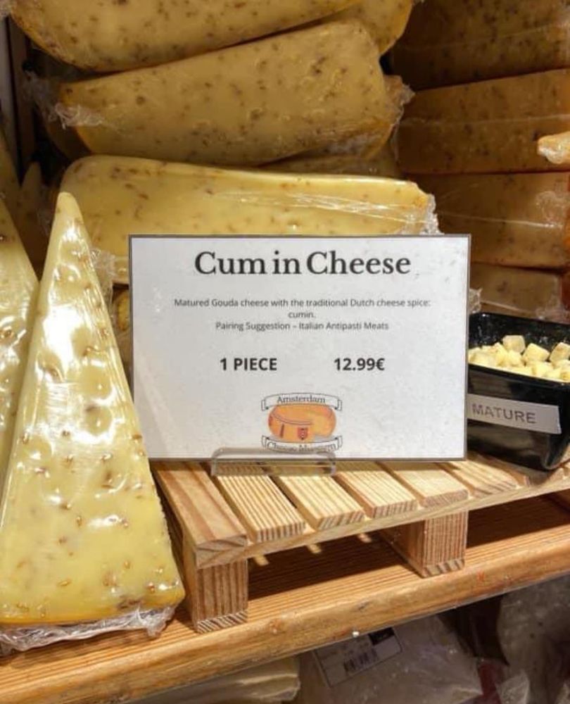 Photo of wedges of pale yellow cheese with dark specks in them.  A sign with poor spacing says "Cum in Cheese", rather than "Cumin Cheese".
