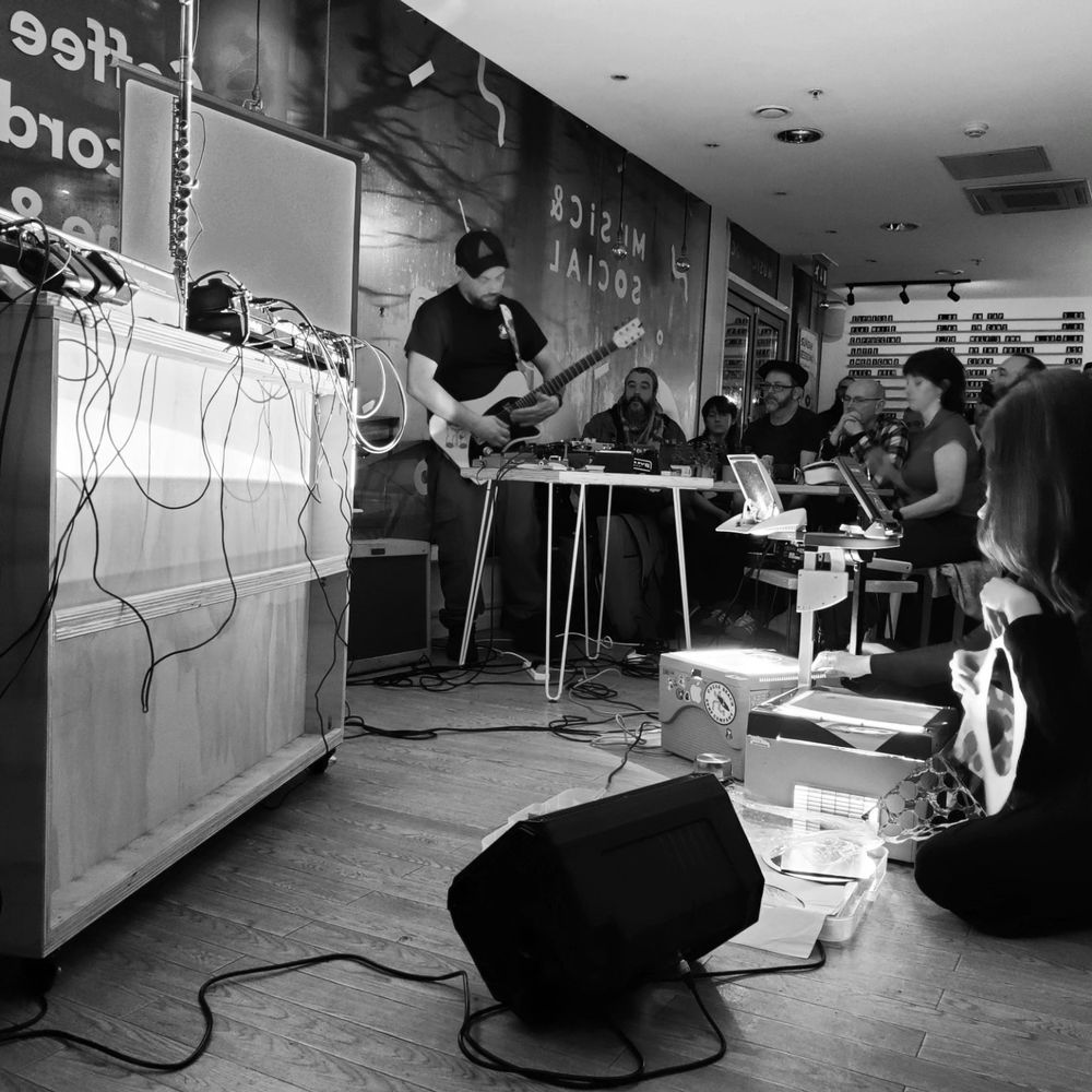 A guitarist improvising whilst two overhead prejectors (OHPs) project lights from the floor