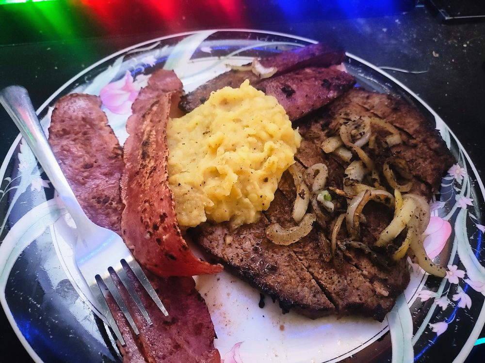 A plate of turkey bacon, sausage, a small steak and hand-made potatoes; resting on an ornate dinner plate. All lovingly crafted by Finn himself 