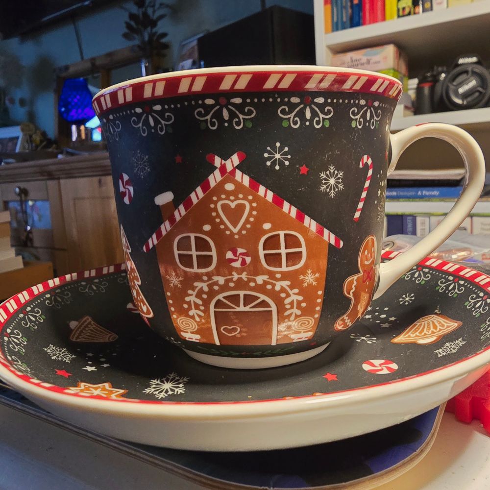 Pictured is a giant mug-sized ceramic tea cup on a giant saucer, decorated in a Christmas style, with gingerbread men, gingerbread houses, gingerbread Christmas trees, with candy canes and bon-bons for pops of colour. There are also white snowflakes scattered all over, as well as red stars and white stars and beautiful curlicues around the edges of the mug and saucer. These fabulous items are made by Easy Life Design, based in Italy, and they have plenty of other wonderful Christmas-style crockery, including this Gingerbread range, which also has matching plates and serving platters. Check it out at:  Gingerbread | Easylife Boutique https://share.google/Z06S4NBbH9H3sBpQp