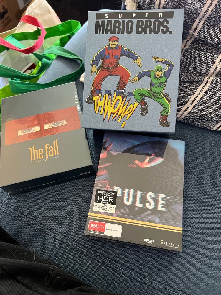 Picture of three 4K movie sets on of loveseat. Super Mario Bros.,The Fall, and Pulse all from Umbrella Entertainment.