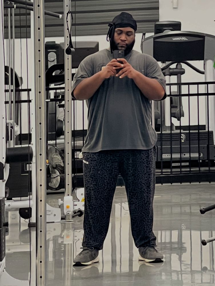 Large beautiful black man covered in oversized grey shirt cans black leopard pans inside of a gym 