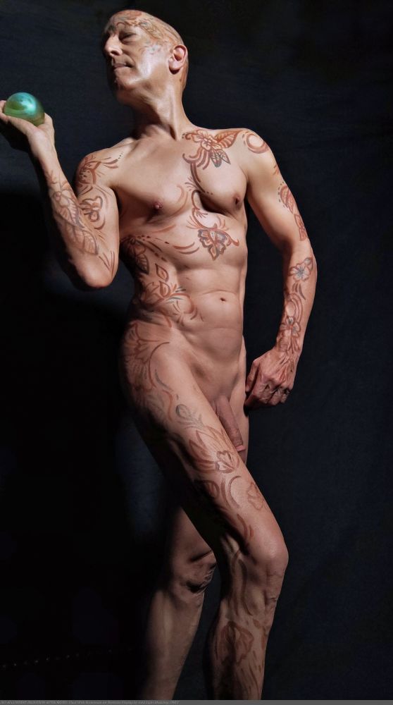 Color photo of nude male model, body painted with a floral themed line design, in a standing pose