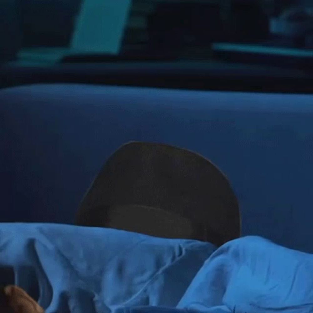 a man wearing a black hat is hiding behind a blue blanket