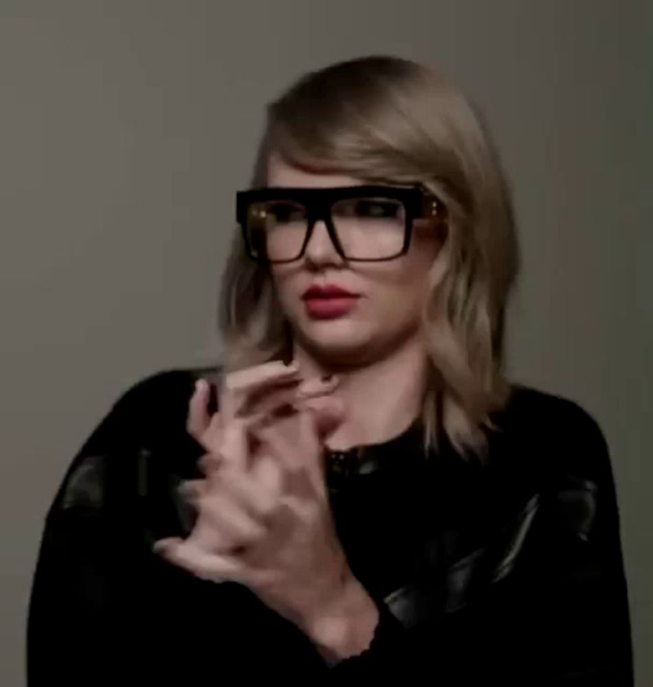 taylor swift is wearing glasses and a black jacket and clapping her hands .