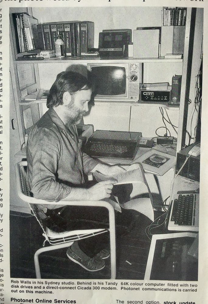 Black and white photo of Rob Walls sitting at studio work-station photographed for New York based pro photographers' magazine with highly modified Tandy Colour Computer and Model 100 portable for a story about communicating worldwide using the NY based photographer network, Photonet.