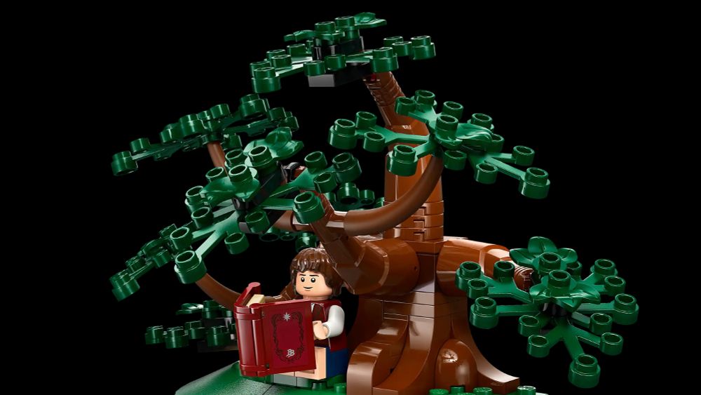 A picture of the Frodo minifigure from the Shire Lego set. He's sitting underneath a Lego tree, reading a giant Lego book.