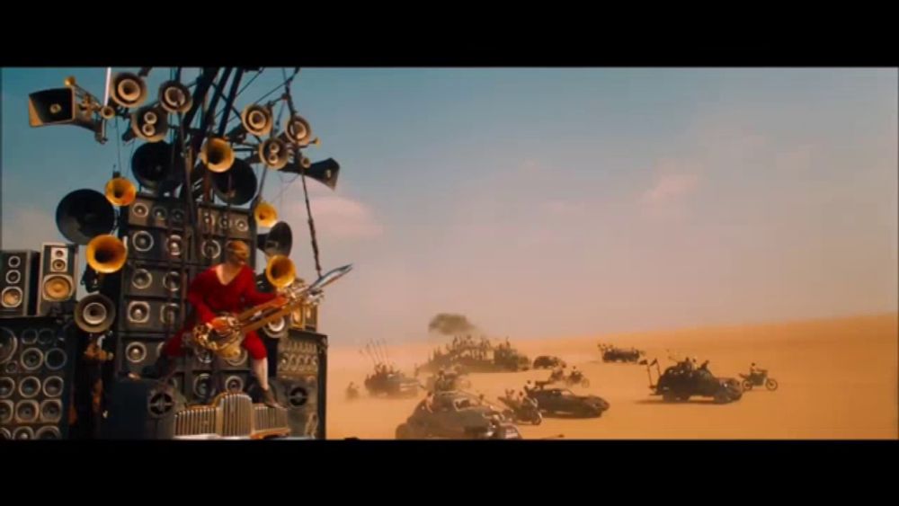 a man is playing a saxophone in front of a wall of speakers in the desert