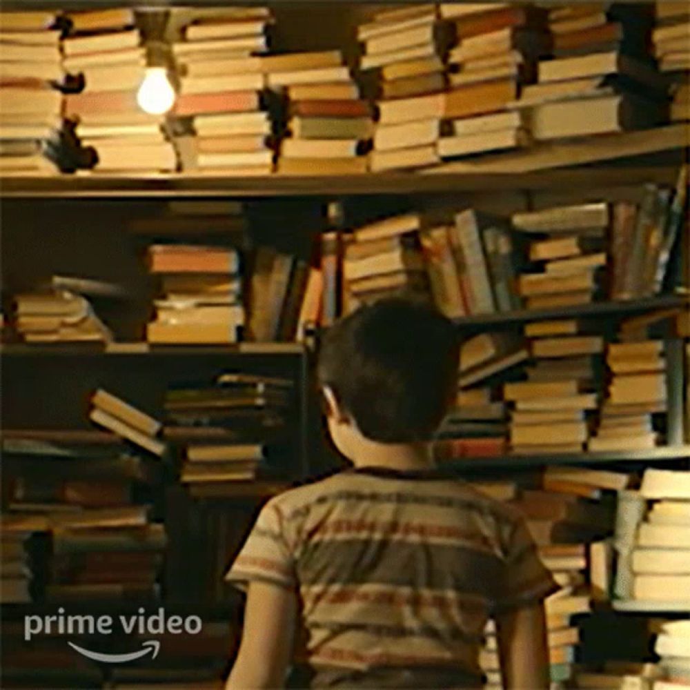 a little boy is standing in front of a bookshelf filled with books .