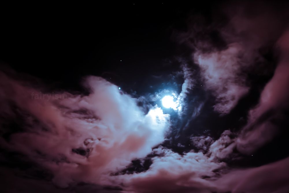 Photograph of the night sky, with the bright illuminated full moon in the center of the frame, and several clouds surrounding it. The moon has no details, and is the only source of light. There is a soft lilac / pink / rose toning to it. 

(Describing colours is hard, because it seems like somehow everyone sees them differently, lol)