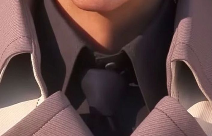 Rufus' tie knot in FFVII Rebirth. It is a firm, three-dimensional knot that angles slightly up to his right at the collar. It has more bulk in the upper half of the knot. The fabric is plain matte black.