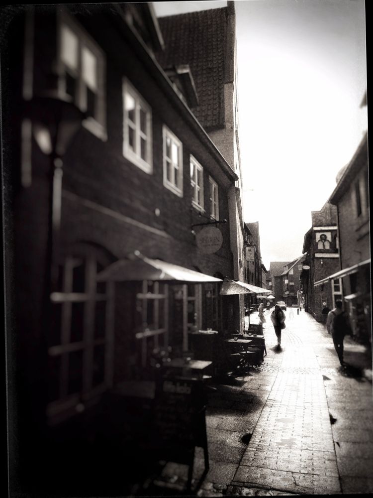 b/w photography of an old town in northern Germany, streets shiny from recent rainfall glistening in blinding light - some people passing by