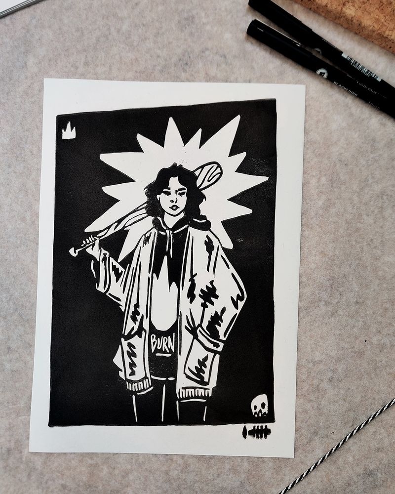 Photo de tirages d'une gravure représentant une personne qui tient une batte de baseball sur son épaule. Elle porte un pull à capuche sur lequel il y a une grosse flamme et écris le mot burn.