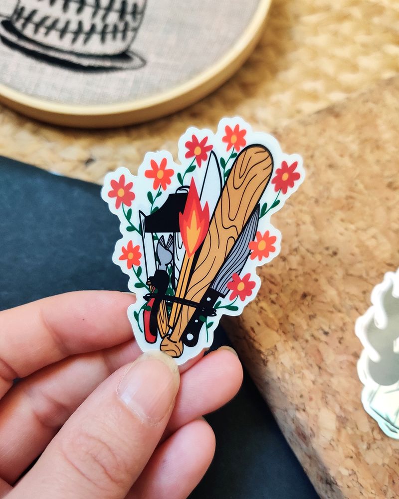 Photo d’un stickers représentant un bouquet un peu particulier puisqu’il est composé d’une batte de baseball, d’une grosse allumette, d’une pince coupante, de trois couteaux, d’un marteau, et de quelques petites fleurs pour agrémenter le tout !