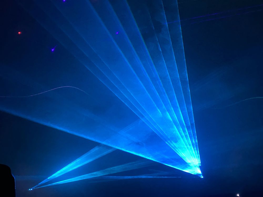 Blue lasers, shooting at angles towards us, the beams visible due to the smoke-filled room