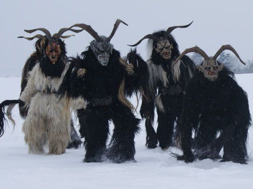 a group of Perchten standing in the snow. they’re dressed in furry sheep skins with big horns and monster masks