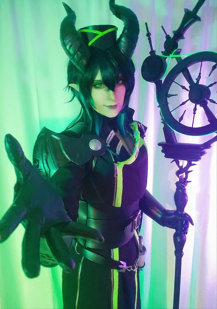 Half body photo of my Malleus cosplay with staff in one hand with the other hand reaching out towards the viewer. 