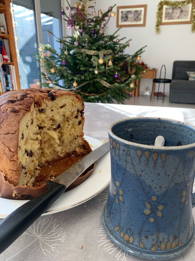Panettone and coffee mug on a table with Christmas tree in the background 🎄