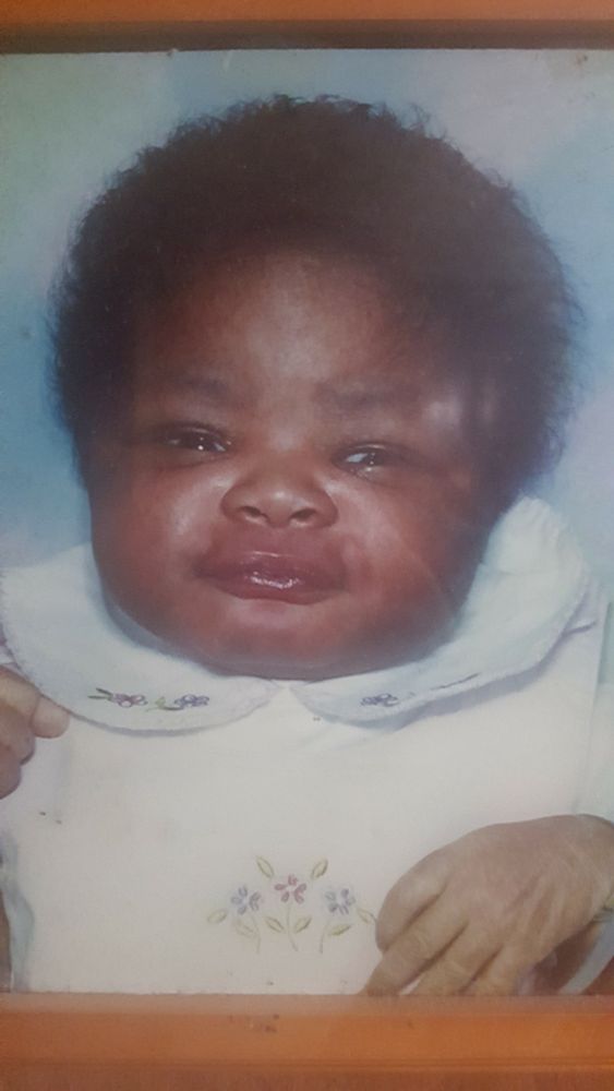 baby me with a small bushy head of hairy and chubby cheeks smiling at the camera. my lightskin limp gay hand is present in the corner foreshadowing my gayness