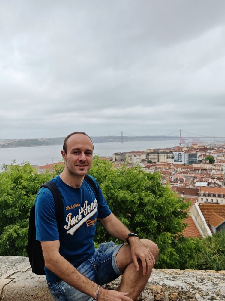 Picture of me on a terrace in Lisbon with a view of Tejo River, the city, and the bridge.