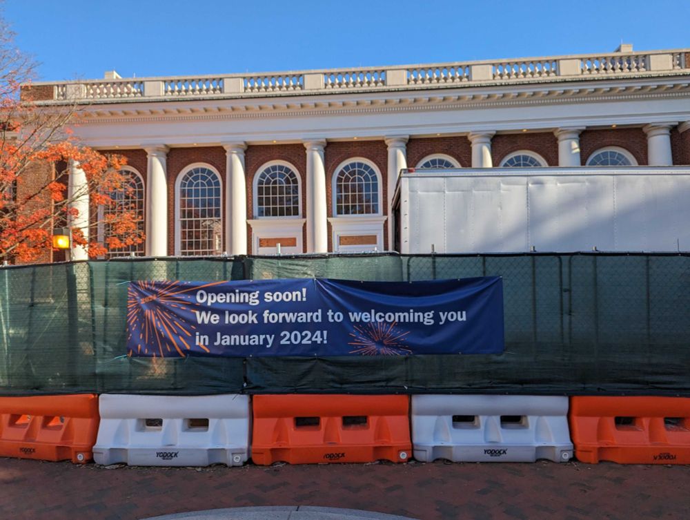 Photo of the side of the University of Virginia's main library, behind construction fencing but with a large "opening soon! we look forward to welcoming you in January 2024!" banner