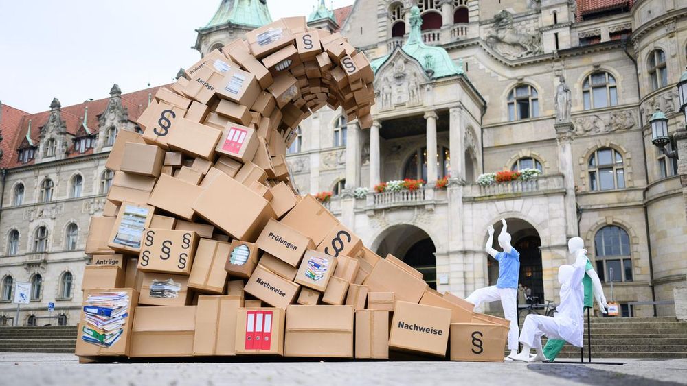 Eine "Bürokratie-Welle" aus Kartons, Aktenordnern, Formularen und Gesetzestexten steht als Symbol für den Bürokratieaufwand im Gesundheitswesen vor dem Neuen Rathaus in Hannover