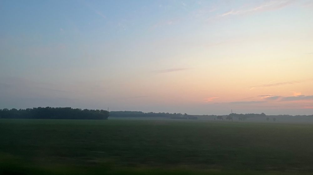 A hazy sunset gradient from blue to red against a green field in the foreground