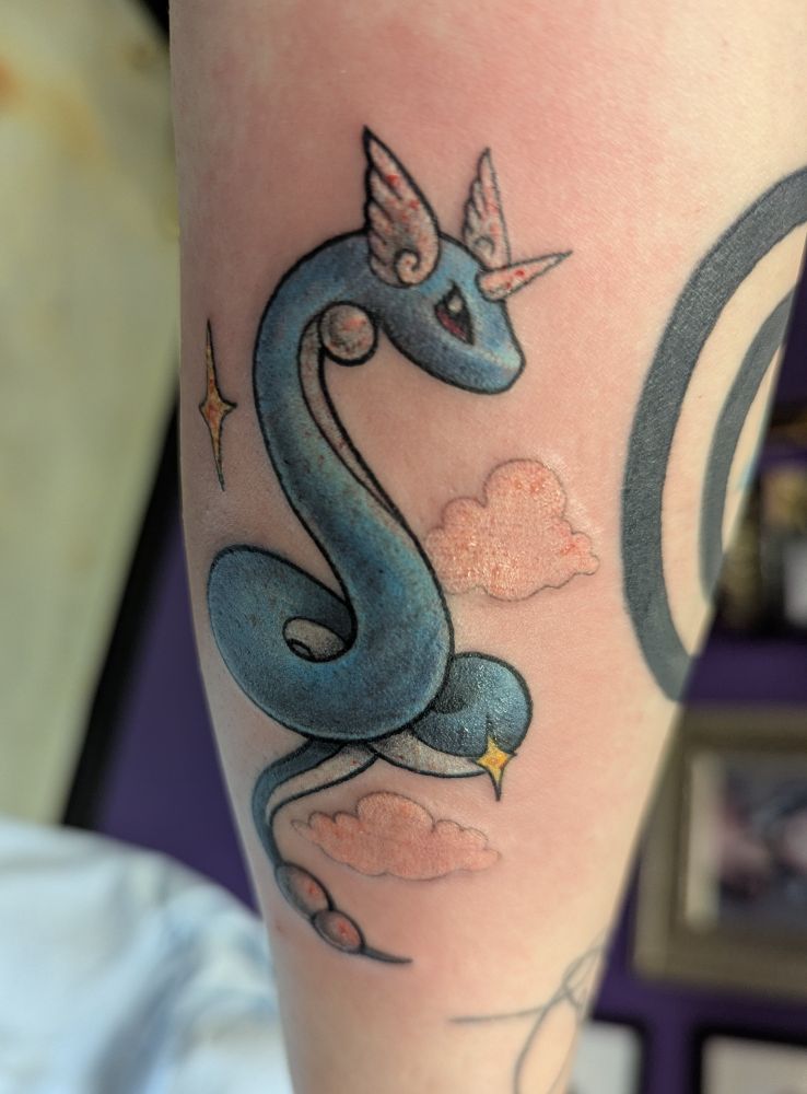 A fresh tattoo of the pokemon Dragonair with an angry eye. There are sparkles and clouds around it