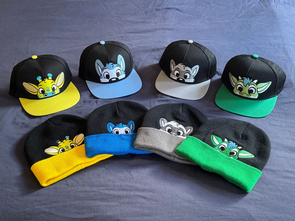 Collection of four beanie hats and four caps featuring the same designs of cartoon animals peeking over the brim. They’re arranged in two curved rows. From left to right there’s a yellow giraffe, a blue husky, a grey raccoon, and a green dragon.