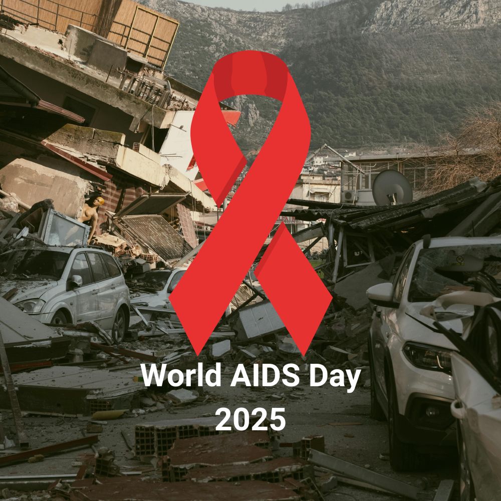 A large red HIV awareness ribbon is overlaid on a street filled with earthquake rubble, damaged buildings, and crushed cars, with mountains in the background. White text at the bottom reads “World AIDS Day 2025”.