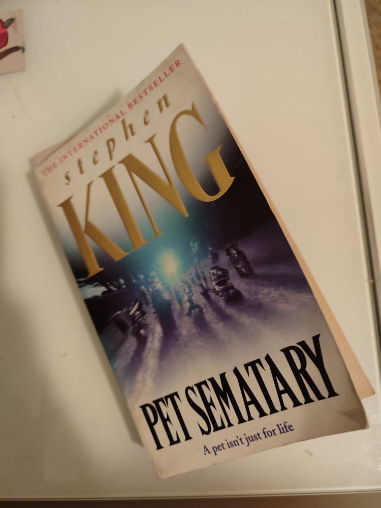 Libro «Pet sematary» (Cementerio de mascotas) de Stephen King sobre una superficie blanca. En la portada se ven unas tumbas en círculos ligeramente desenfocadas en blanco y negro.