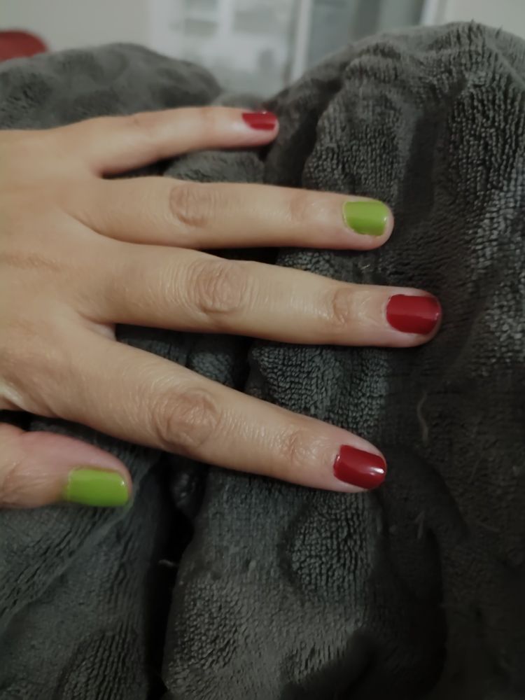 Sobre una manta marrón calentita, se ve una mano con las uñas de colores navideños: una verde, dos rojas, una verde y una roja.