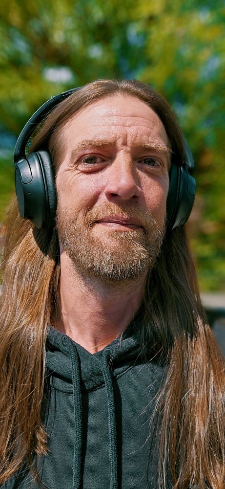 Man (Brent Lee) with long hair, wearing headphones, looking pleased.